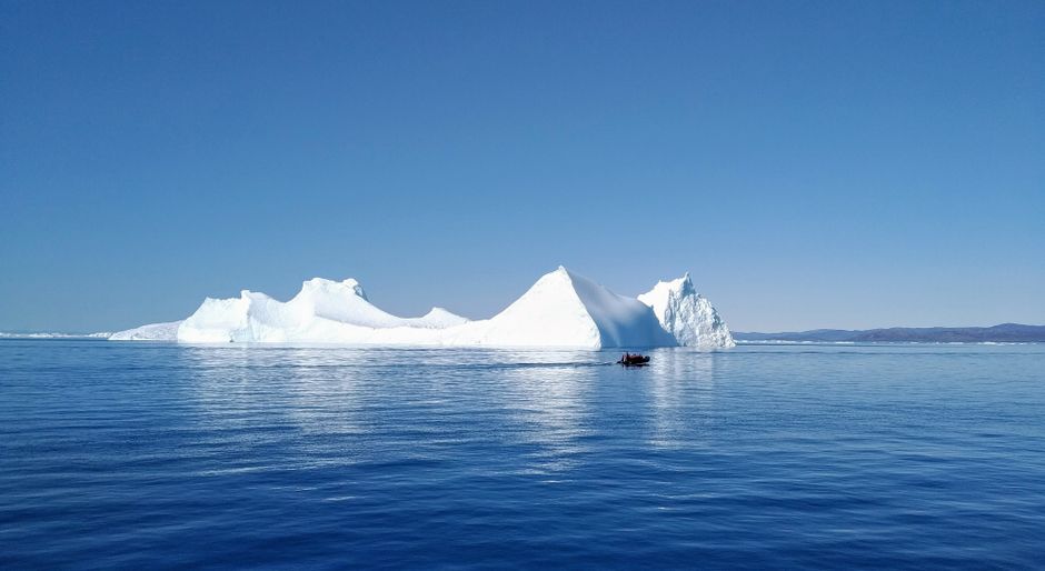 A serene scene of an iceberg with a small boat in the waters of Ilulissat, Greenland.