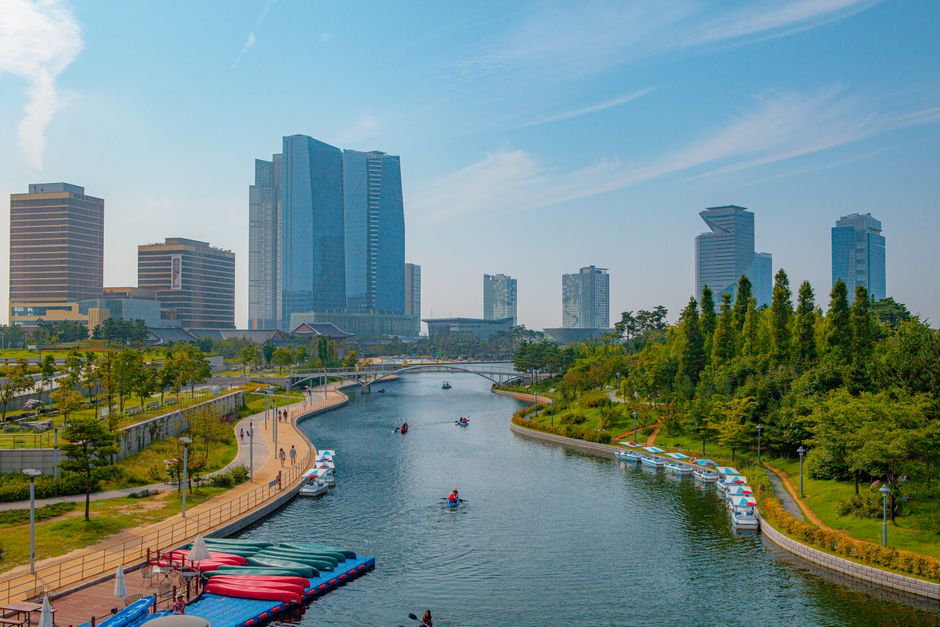 A scenic view of a modern urban skyline with a river flowing through a park in Incheon, South Korea.