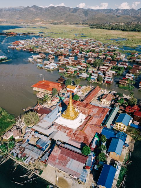 Stunning aerial view of a floating village and golden pagoda in Shan, Myanmar, with scenic mountain backdrop.