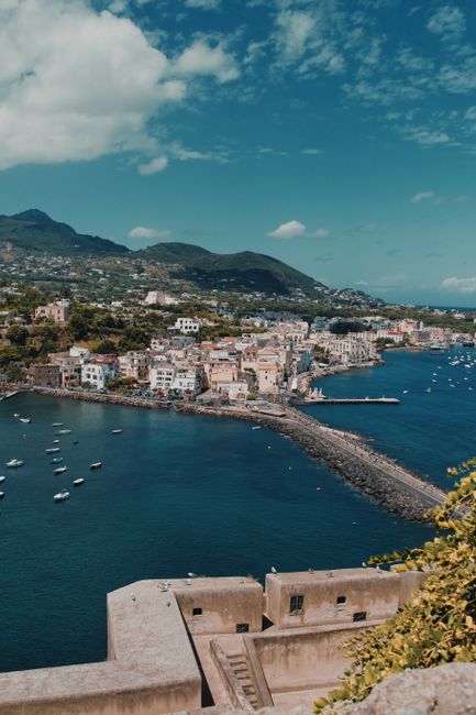 A breathtaking aerial shot of Ischia Porto, Italy, showcasing the harbor and hills under a clear blue sky.