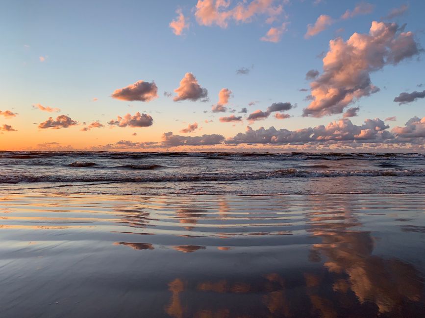Vibrant sunset reflection over the Baltic Sea shoreline with colorful clouds and calm waves.