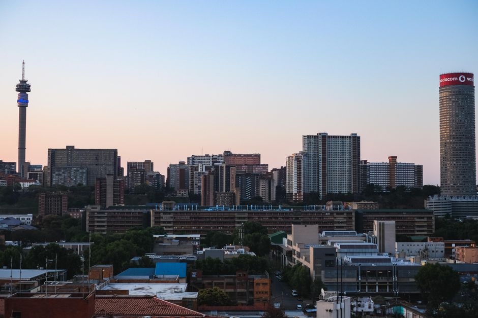 A panoramic view of Johannesburg cityscape during sunset, featuring modern skyscrapers and iconic towers.