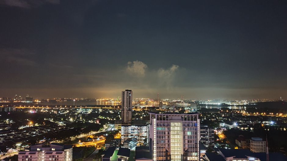 A vibrant night view of the Johor Bahru skyline with illuminated city lights and clear sky.
