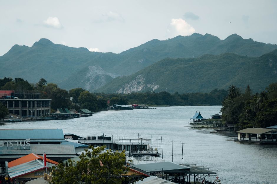 Picturesque view of the riverside in Kanchanaburi, Thailand, with mountains in the background.