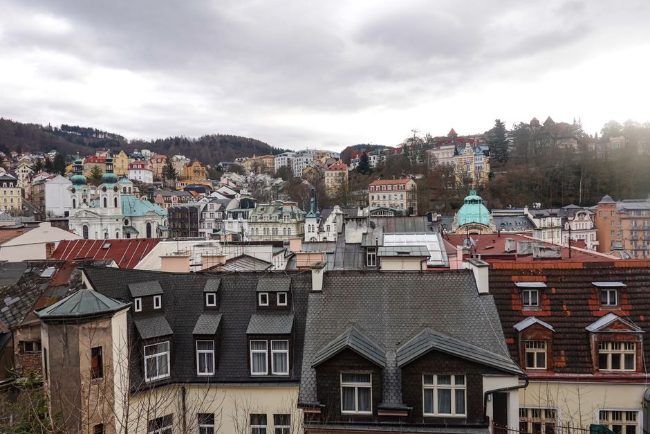 A scenic view of Karlovy Vary's historic buildings amidst lush hills on a cloudy day.