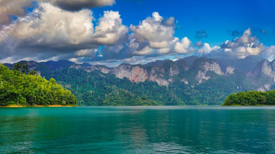 Breathtaking view of a serene lake and majestic mountains under a cloudy sky in Surat Thani, Thailand.