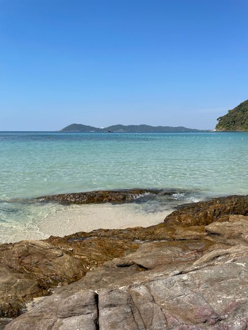 Serene view of a pristine beach and rocky shore in Rayong, Thailand, under a clear blue sky.