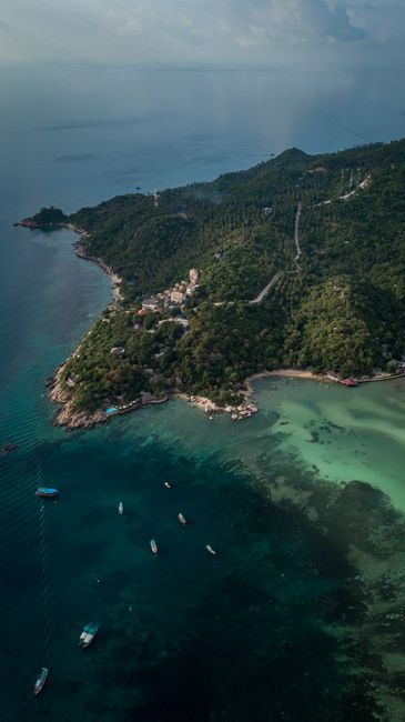 Breathtaking aerial shot of a tropical island coastline in Thailand featuring lush greenery and clear blue waters.