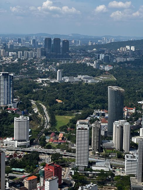 Stunning aerial view of Kuala Lumpur's urban skyline and lush greenery under a clear blue sky.