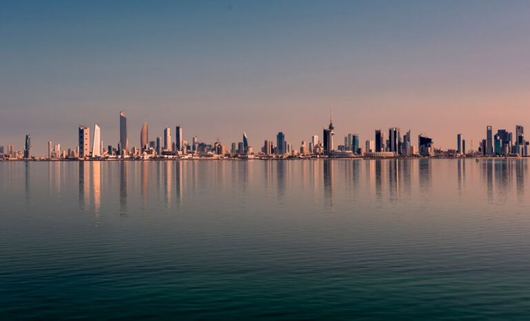 Beautiful Kuwait City skyline reflected on calm water at sunset, showcasing modern architecture.