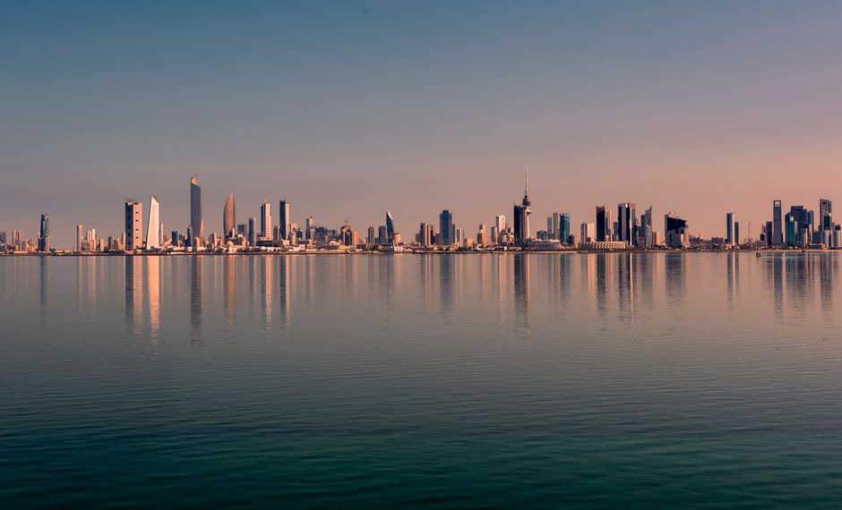 Beautiful Kuwait City skyline reflected on calm water at sunset, showcasing modern architecture.