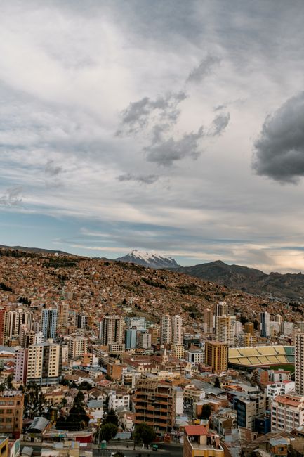Explore the stunning aerial view of La Paz with its vibrant cityscape set against majestic mountains under a cloudy sky.