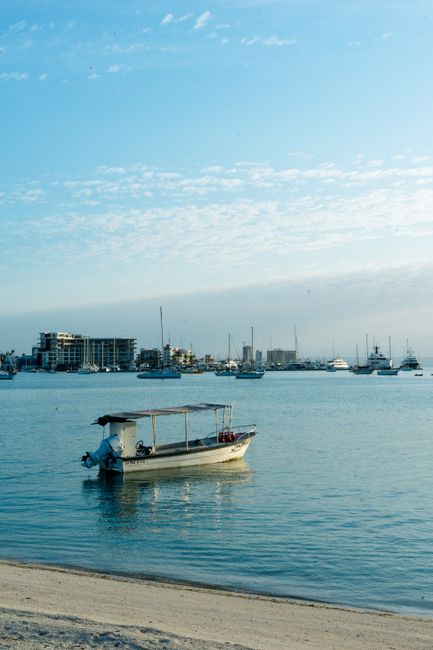 Serene beach view of a dinghy and boats at La Paz, Baja California Sur, Mexico, under a clear summer sky.