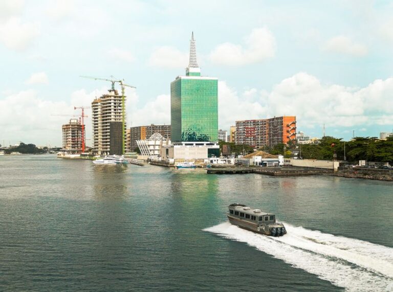 Scenic view of Lagos skyline featuring modern buildings and a motorboat in the lagoon under a bright sky.