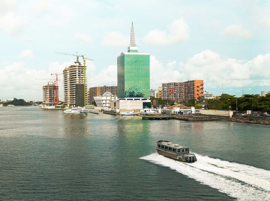 Scenic view of Lagos skyline featuring modern buildings and a motorboat in the lagoon under a bright sky.
