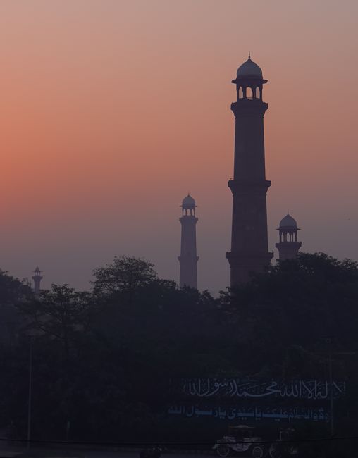 A moody silhouette of minarets and trees enveloped in fog during a vibrant sunset.