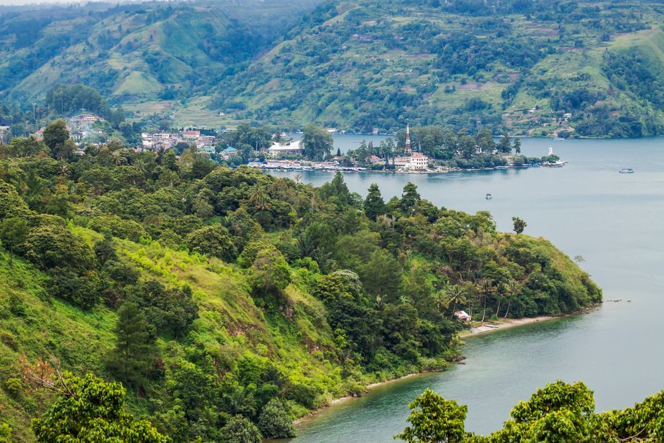 Lush green hills overlooking a serene lake with a distant village. Perfect for travel and nature enthusiasts.