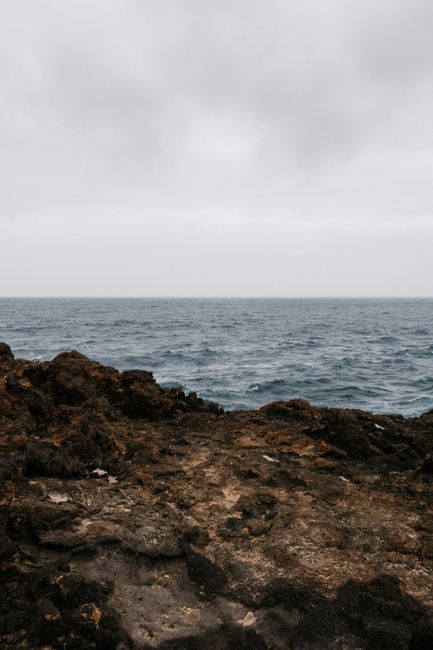 A rocky coastal landscape with a dramatic overcast sky over the sea.