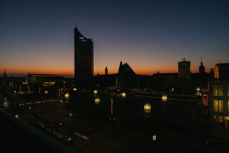 Dusk view of Leipzig's skyline with city lights and orange twilight sky.