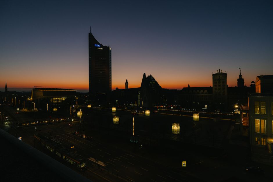 Dusk view of Leipzig's skyline with city lights and orange twilight sky.