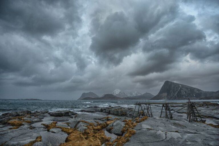 Stormy clouds over the rugged Nordland coastline create a dramatic seascape with mountains in the distance.