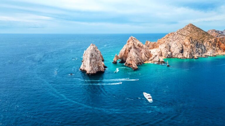 Stunning aerial shot of Cabo San Lucas Arch with vibrant blue ocean and boats in view.