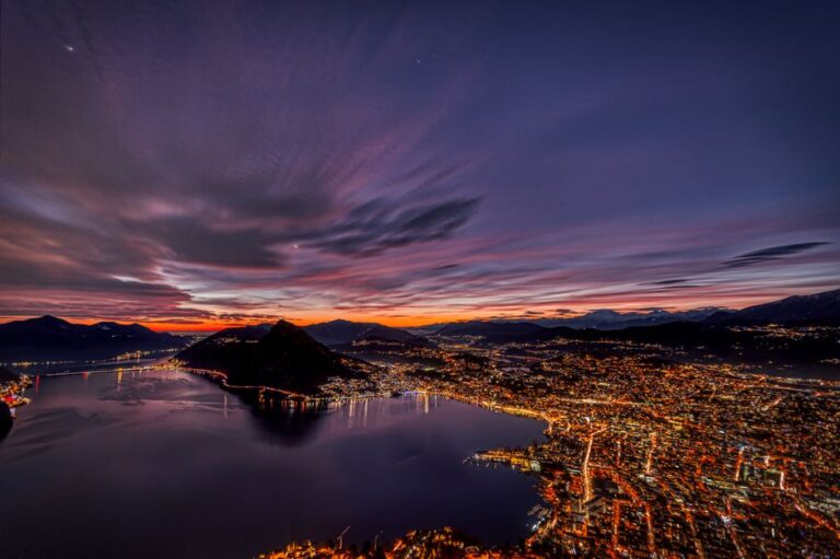 Mesmerizing aerial shot of Lugano city lights reflecting on the lake at twilight.