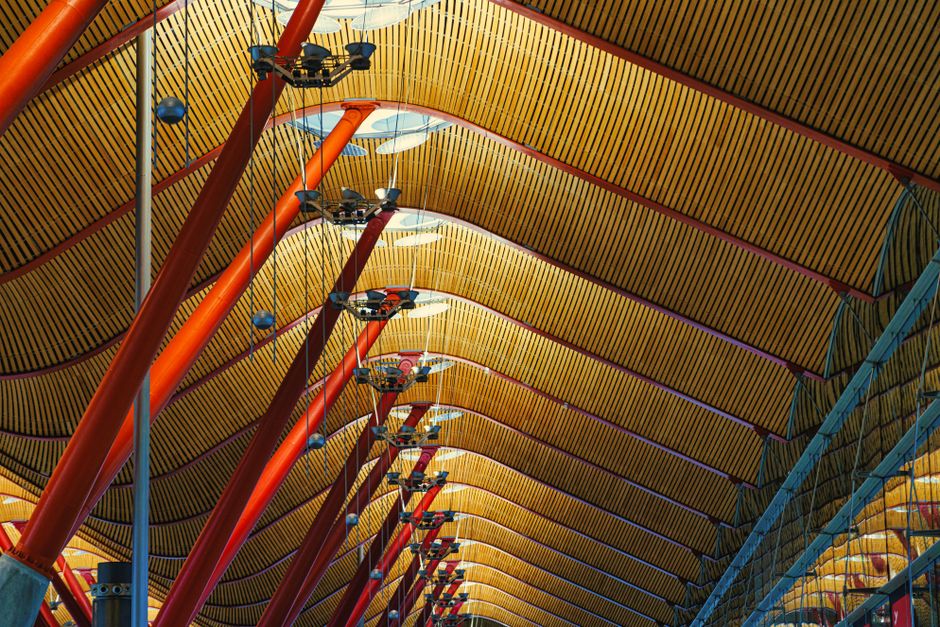 Intricate ceiling design of Madrid Barajas Airport with red poles and geometric patterns.