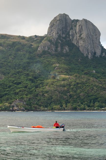 Explore the stunning coastal landscapes of Fiji with a lone boat on calm waters and a majestic mountain backdrop.