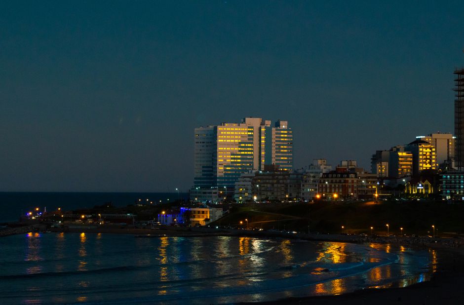 A vibrant skyline view of Mar del Plata, Argentina at twilight with city lights reflecting on the sea.