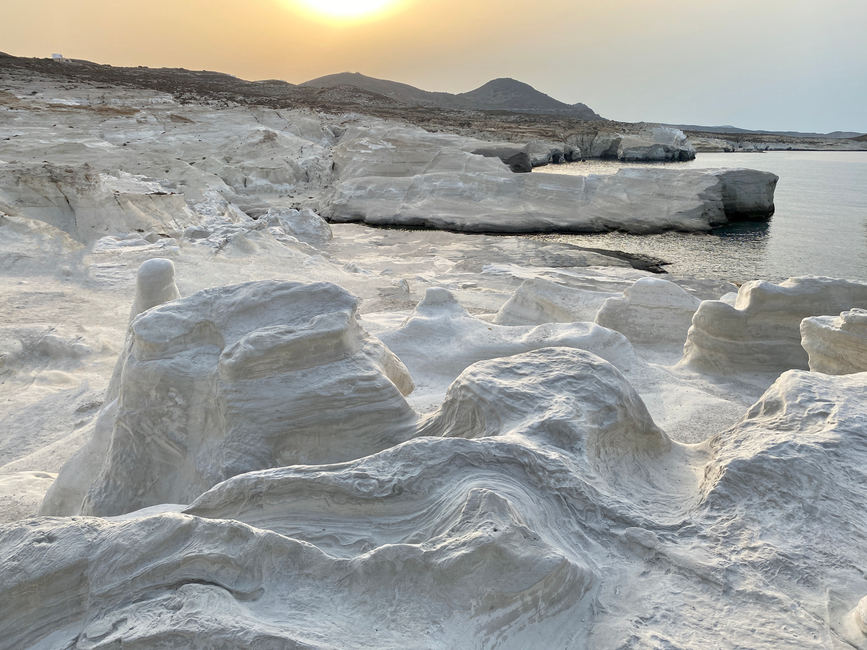 Explore the unique white rock formations of Sarakiniko Beach in Milos, Greece during a serene sunset.