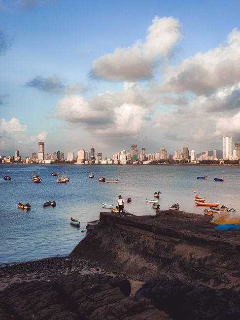 Boats scattered on a peaceful bay with a bustling city skyline and fluffy clouds above.