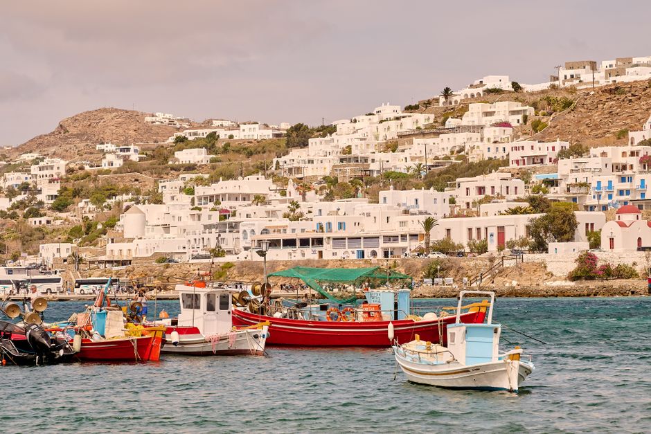 Charming white buildings and vibrant boats in Mykonos harbor on a sunny summer day.