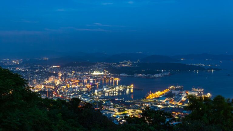 Dazzling evening view of Nagasaki harbor with illuminated cityscape and vibrant shipping terminals.