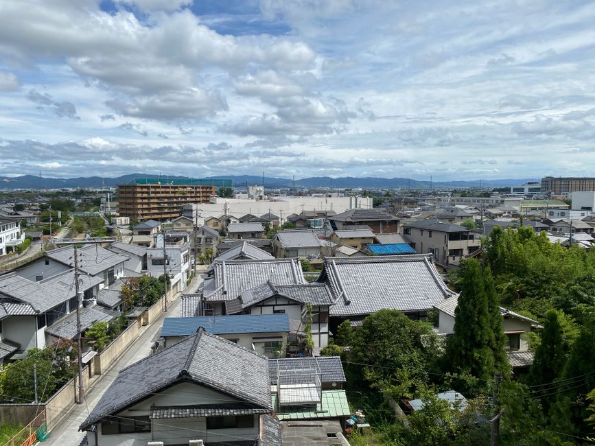 An aerial view of traditional Japanese homes with tiled roofs, set against a backdrop of mountains under a cloudy sky in Nara, Japan.