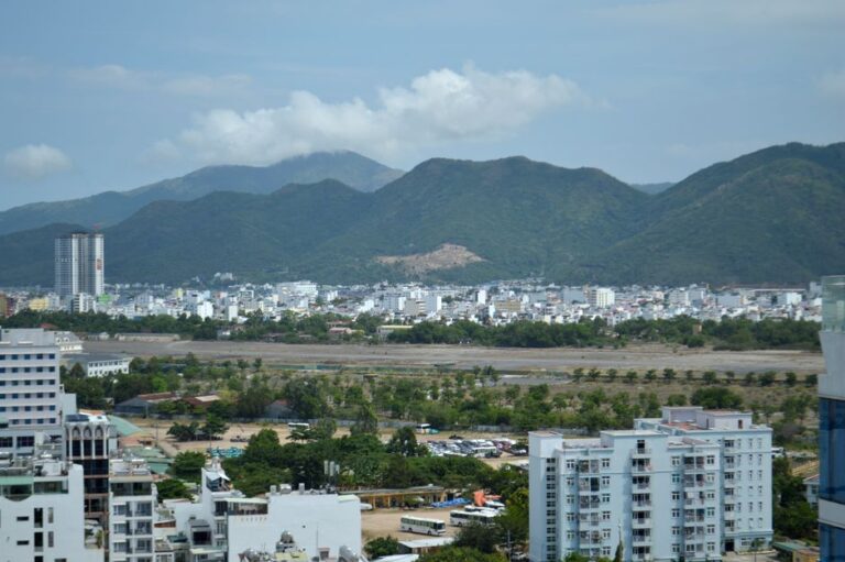 Skyline view of a city framed by lush mountains under a blue sky.