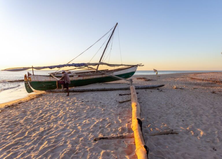 A serene beach scene in Madagascar with a traditional fishing boat during sunset on the sandy shore.