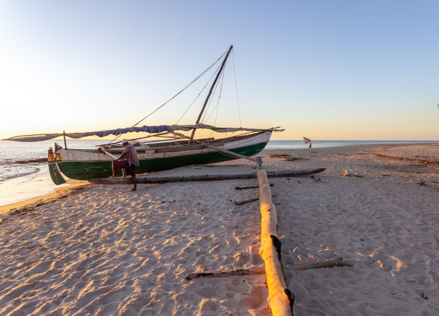 A serene beach scene in Madagascar with a traditional fishing boat during sunset on the sandy shore.
