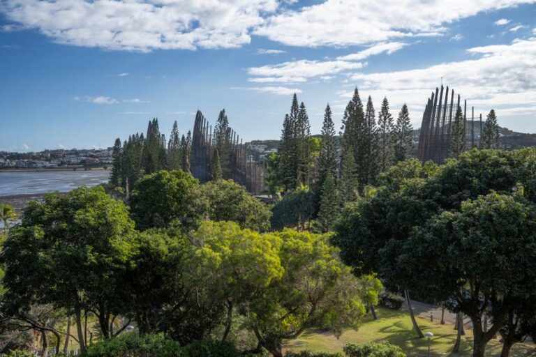 A scenic view of the Tjibaou Cultural Center with lush greenery and cloud-streaked sky in Nouméa.