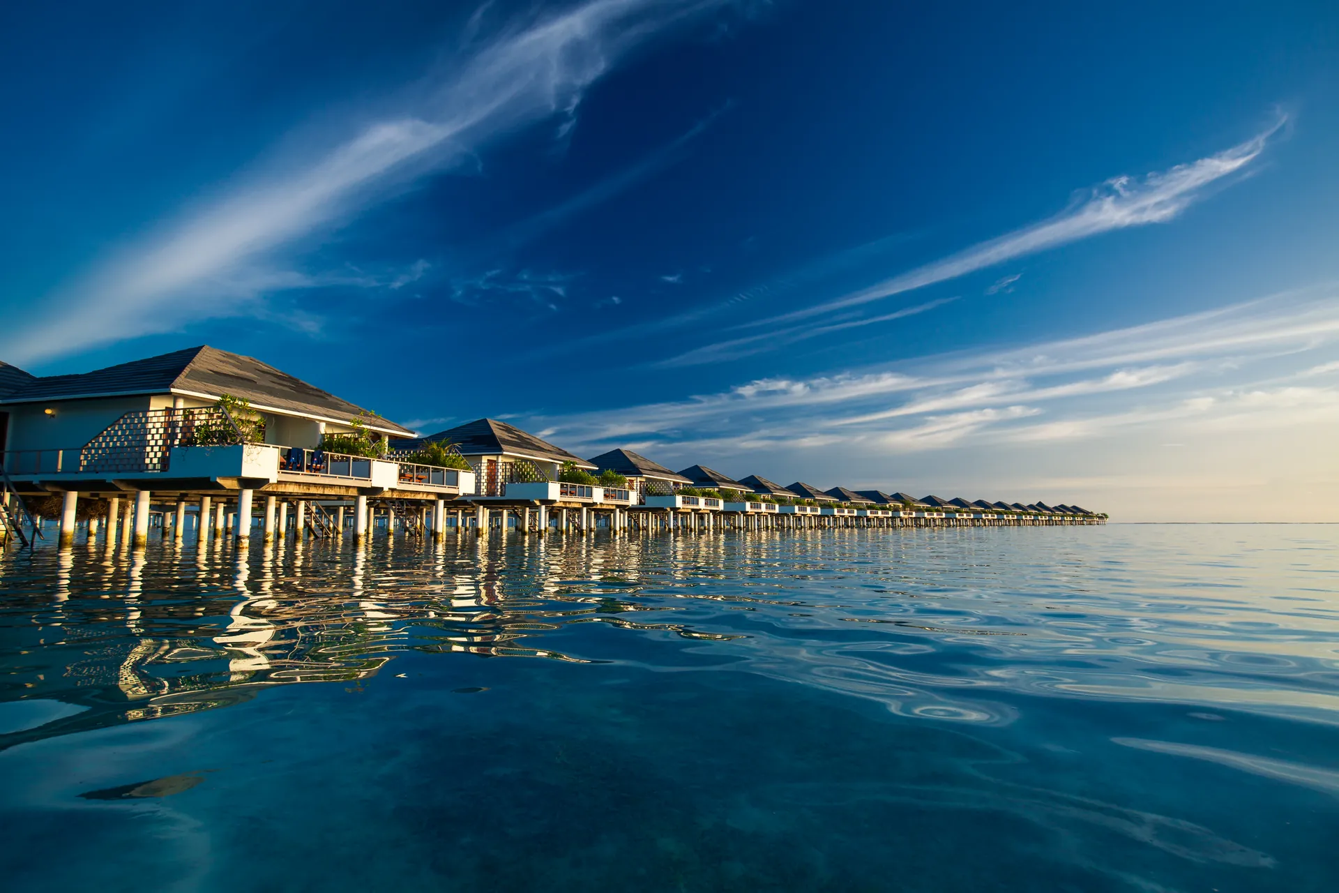 Overwater villas reflected in a calm blue lagoon in the Maldives