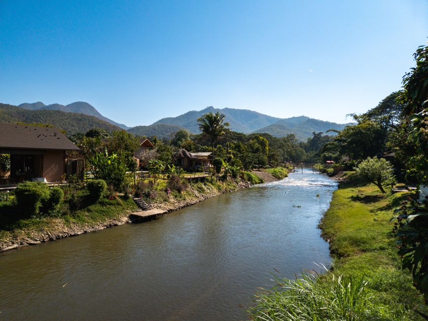 Tranquil riverside village nestled in lush mountains under a clear blue sky.