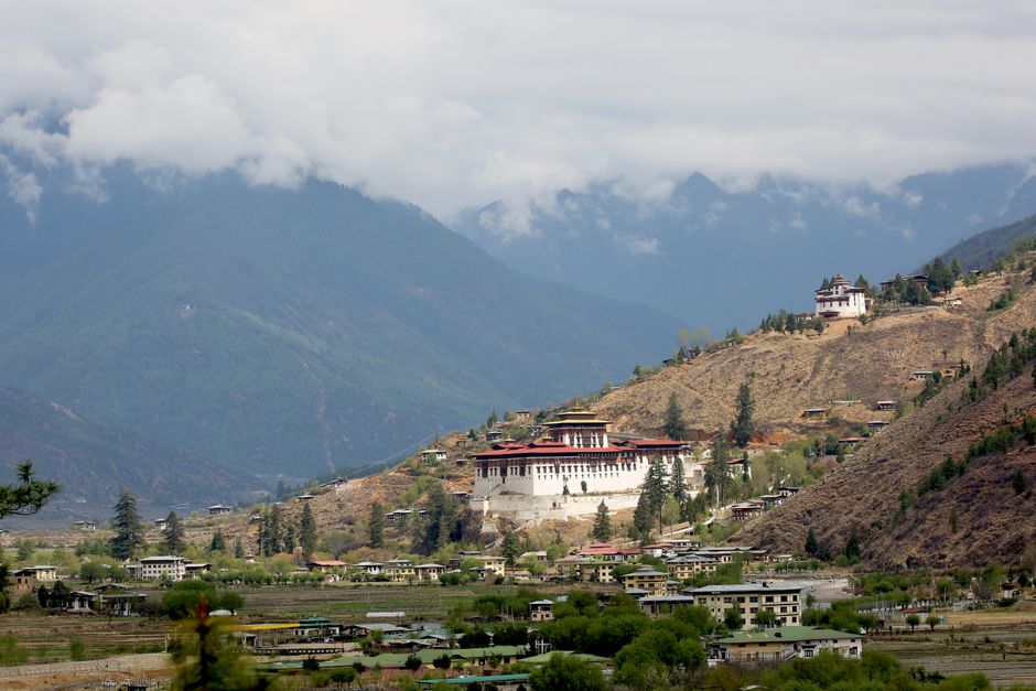 Scenic view of Paro Valley with Rinpung Dzong, surrounded by mountains and clouds in Bhutan.