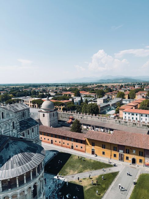 Aerial shot of Pisa showcasing its historic architecture and landscape under clear blue skies.
