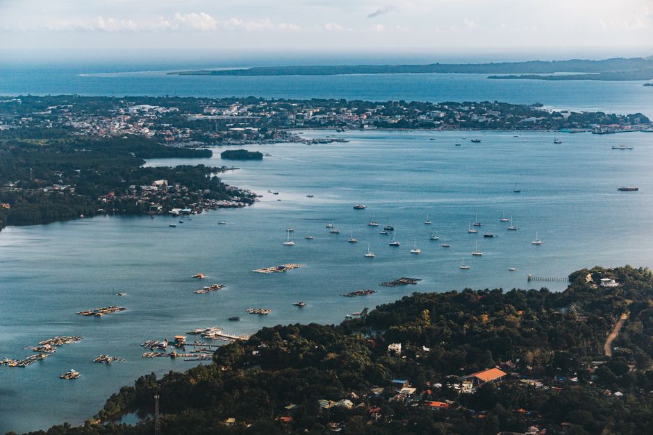 Stunning aerial view of a coastal city with sailboats dotting the bay, displaying vibrant scenery and serene waters.
