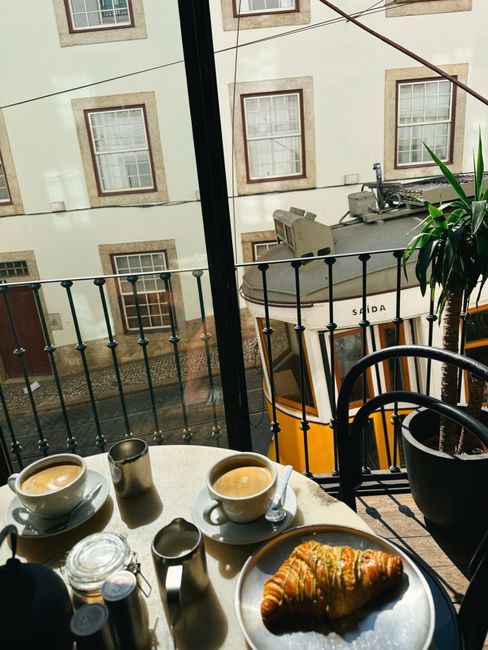 Sunny breakfast scene with coffee and croissant by Lisbon tram window view.