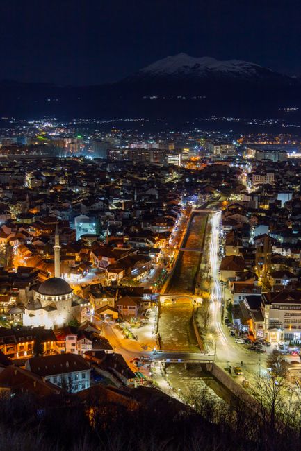Captivating aerial shot of Prizren at night showcasing illuminated cityscape and distant mountains.