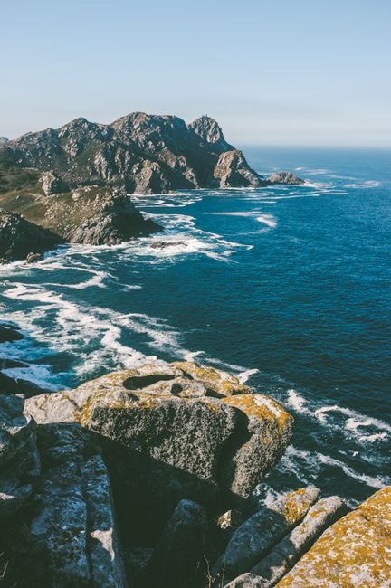 Breathtaking view of the rocky coastline in Galicia, Spain with waves crashing against the cliffs under a clear blue sky.