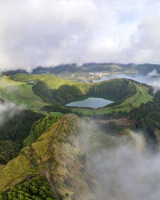 Stunning aerial view of Sete Cidades Crater Lake, lush green landscapes, and misty clouds in Azores.