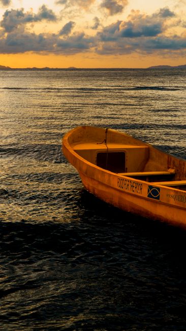 A boat drifting on the serene waters of Tela, Honduras at sunset, capturing the golden hues and peaceful ambiance.