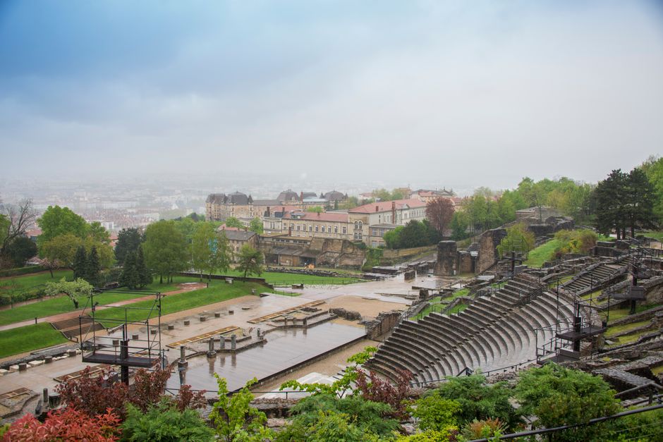 View of the ancient Roman amphitheater in Lyon with surrounding cityscape, cloudy sky.